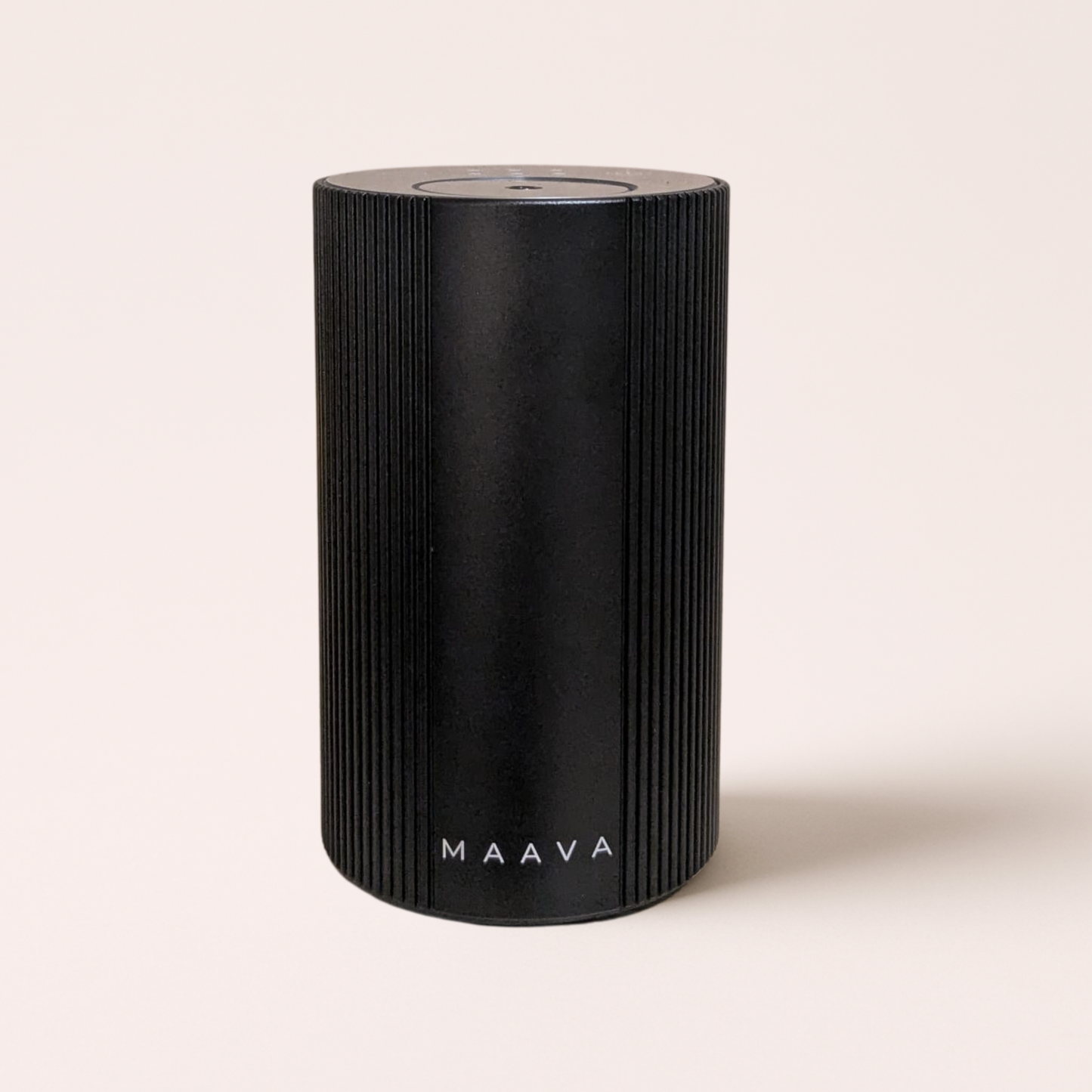 A black cylindrical portable speaker with vertical ridges and the brand name 'MAAVA' printed in white near the bottom, set against a solid light beige background.